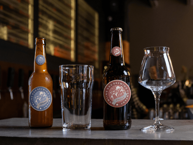 Howling Dog Brewing bottle mock-up with clear glasses of Pilsner and Porter beers. Logo and branding design.